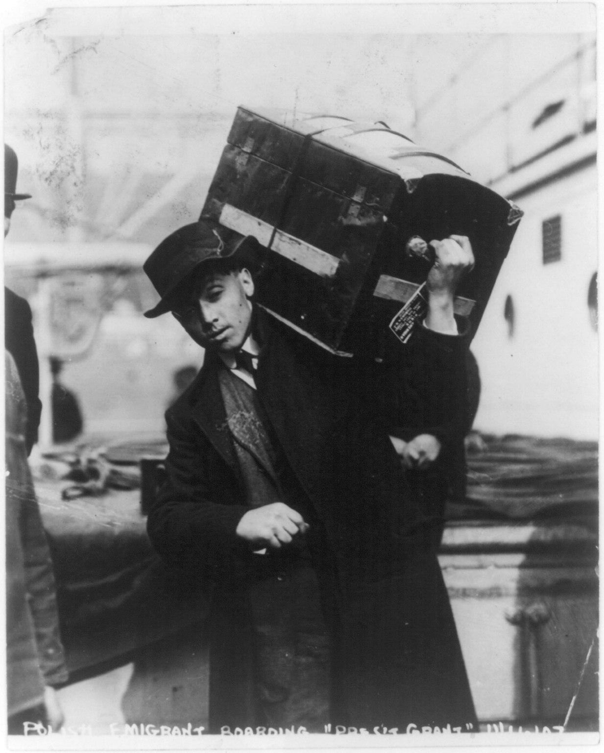 Historic black-and-white photograph of a Polish emigrant carrying a trunk while boarding a ship, 1907