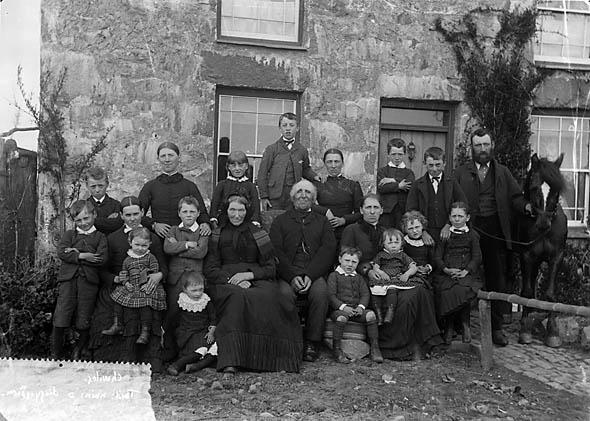 An archival photograph of a large family outside a house in Chwilog, Wales, around 1885